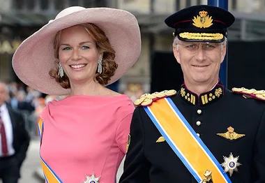King and Queen of Belgium in ceremonial attire, smiling at an event.
