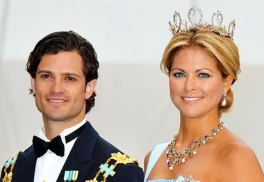 Prince and princess in formal attire at a ceremonial event, with the princess wearing a tiara and necklace.