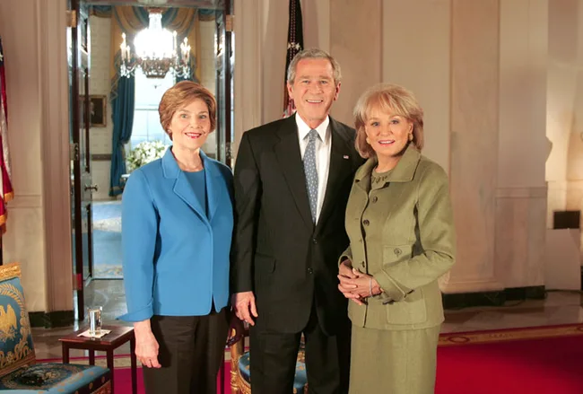 Three people standing in a formal room with chandeliers and elegant decor.