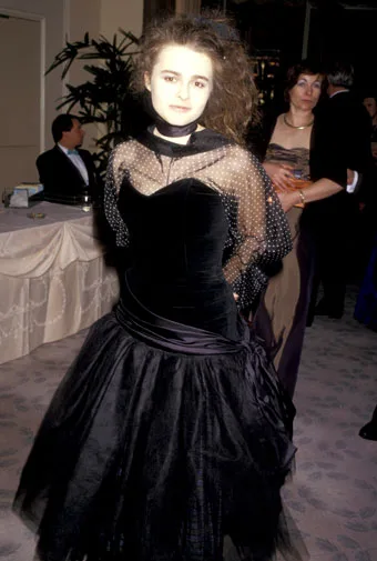 A woman in a black gown with sheer polka dot sleeves at an indoor event.