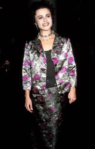 A woman in a floral outfit smiles, facing forward, against a dark background.