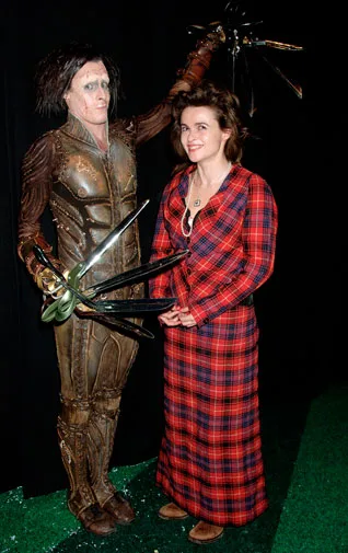 A person in a red plaid dress stands next to an Edward Scissorhands figure in a brown costume with scissor hands.