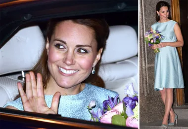 A woman in a light blue maternity dress holds a bouquet, smiling and waving from inside a car.