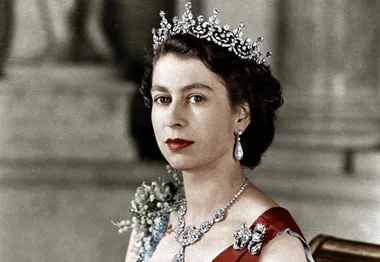 A woman wearing a tiara and formal attire, adorned with jewelry, looking poised and regal.