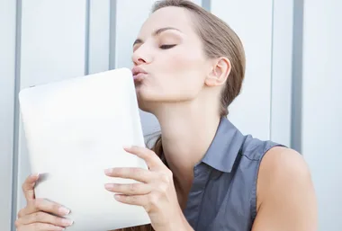 Woman lovingly kisses a tablet, expressing affection for technology.
