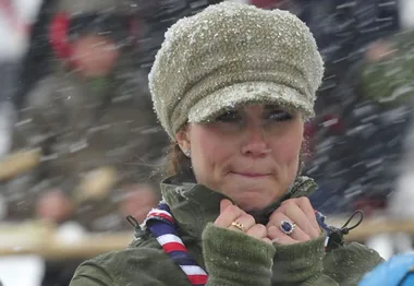 A woman in a snow-dusted hat and scarf braces against the cold at an outdoor event.