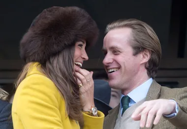 A woman in a yellow coat and fur hat smiles at a man in a suit, both appearing joyful and engaged in conversation.