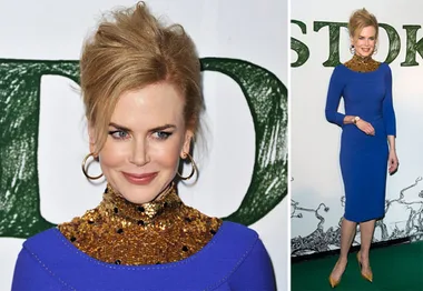 Nicole Kidman in a blue dress with a gold sequined neckline at an event, smiling and standing on a green carpet.