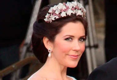 A woman wearing an elegant tiara with pink gems and floral design, smiling slightly, hair styled in an updo.