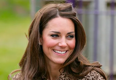 A smiling woman with long brown hair, outdoors, wearing a patterned coat.