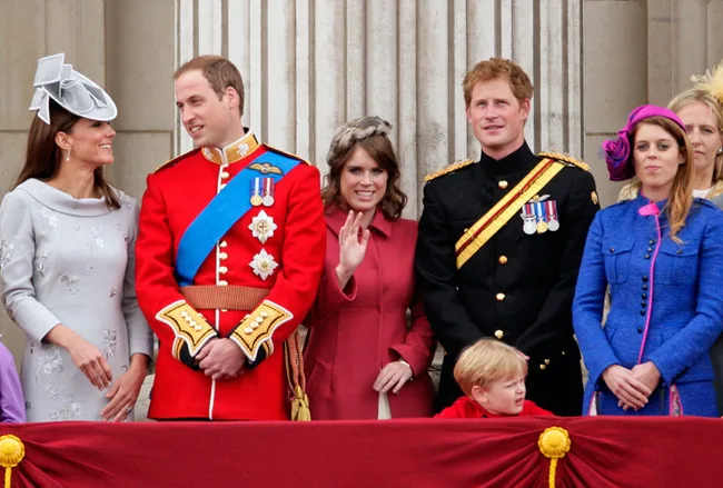 A group of royals, including adults in formal attire and a child, stand on a balcony at a public celebration.
