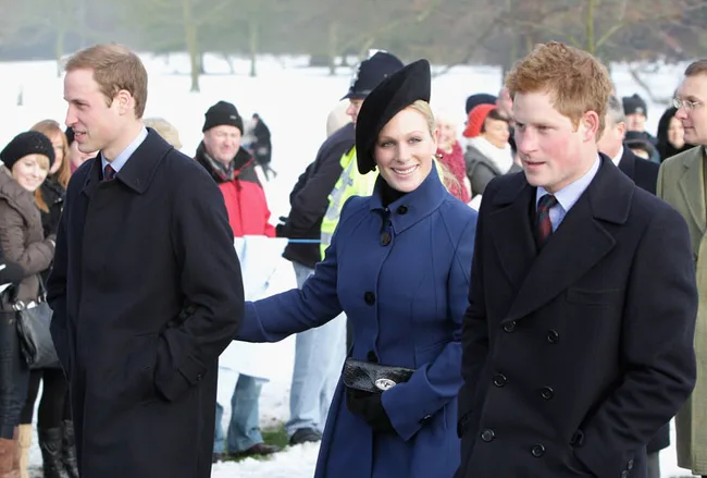 Three people in winter coats walking outside in the snow, with a group of others in the background.
