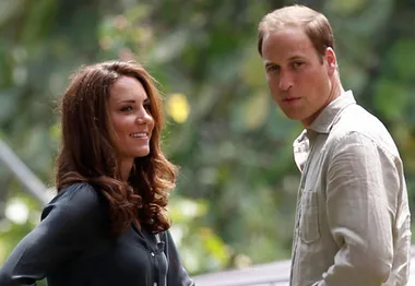Two people outdoors smiling and looking in the same direction, surrounded by greenery.
