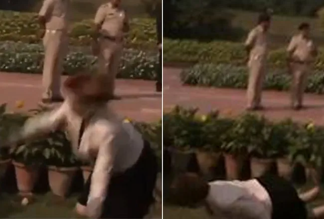 A person falls near potted plants in front of two standing uniformed officers.