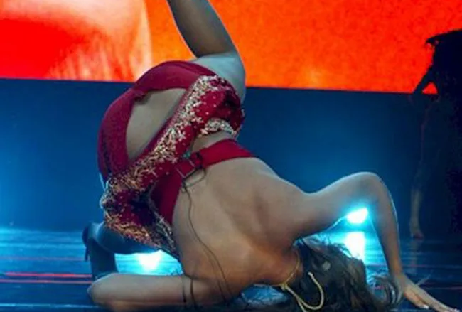 A dancer in a red outfit strikes a dramatic pose on stage with colorful lighting in the background.