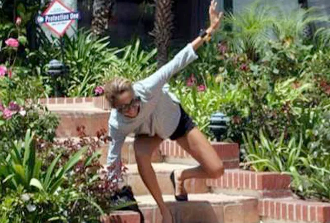 Person stumbling down brick stairs surrounded by greenery and flowers.