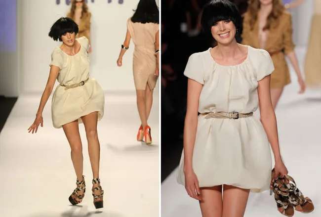 Model wearing a short beige dress stumbles but smiles while walking on a fashion runway.