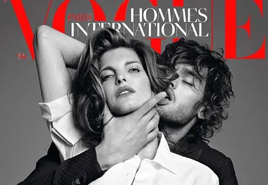 A man and woman pose on the Vogue Paris Hommes International cover, with the man's hand on the woman's face, in grayscale.