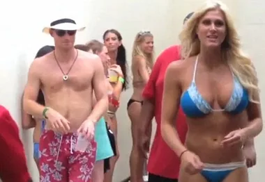 Shirtless man in hat and red trunks at beach party with women in bikinis.