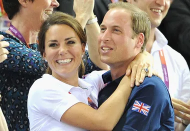 A couple embraces and smiles among a crowd, with a British flag on a sleeve.