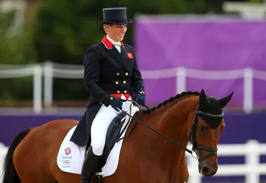 Rider in formal attire on a horse during an Olympic equestrian event.