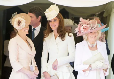Women in elegant dresses and hats smiling and standing together at a formal event.