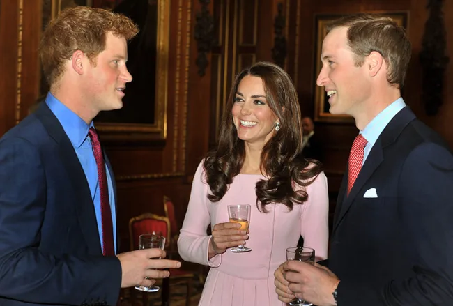 Three people in formal attire holding drinks, smiling, and chatting in an elegant room with ornate decorations.