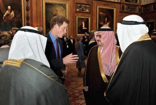 Group of men in formal attire conversing in an ornate room with framed paintings on the walls.