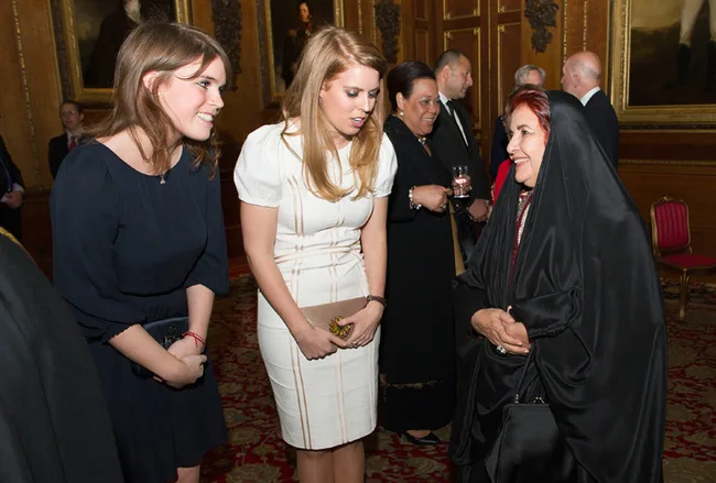 Two women in formal dresses talking to an older woman in traditional attire at a social event.