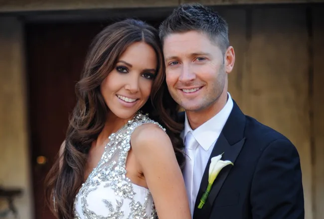 A couple in formal attire smiling, with the woman wearing a sequined dress and the man in a suit with a white boutonniere.