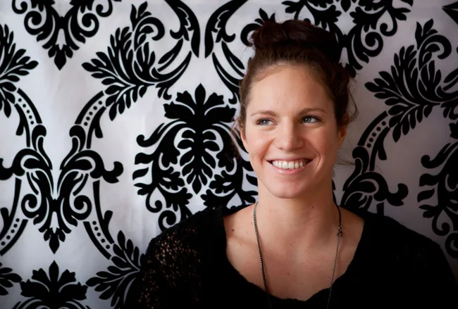 A woman with a bun hairstyle smiles warmly against a patterned black and white background.