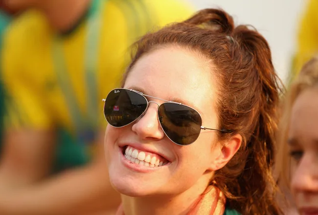 Smiling woman wearing sunglasses and a ponytail, in a yellow and green sports setting.