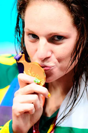 Swimmer in a colorful tracksuit kisses a gold medal with a design featuring a fish.