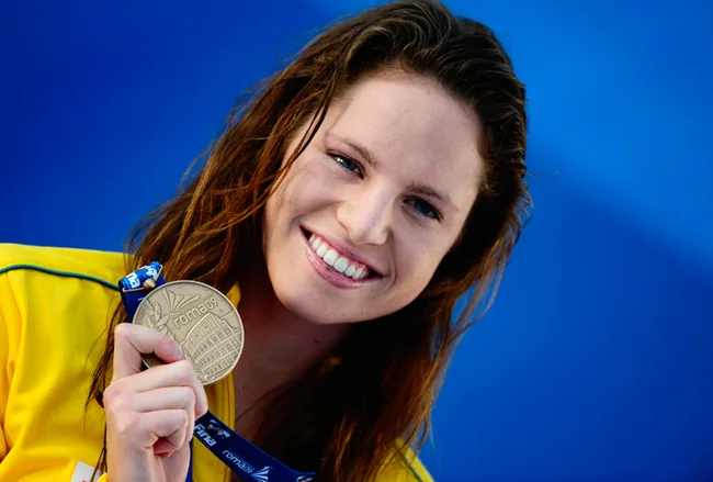 Woman smiling and holding a silver medal against a blue background.
