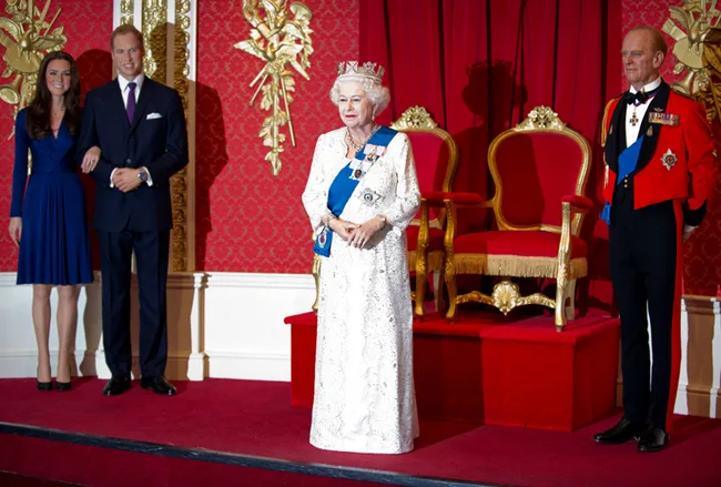 Wax figures of four royals, including two women and two men in formal attire, standing in a regal setting.