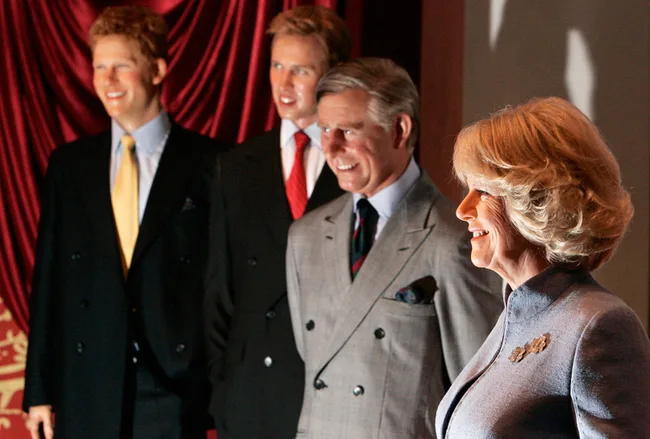Four wax figures of people in formal attire, standing in front of red curtains, smiling.
