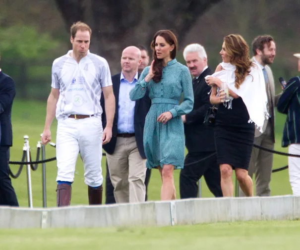 Group of people walking on a polo field, one in a polo outfit and others in formal attire, including a woman in a green dress.