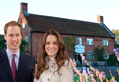 Royal couple posing in front of a historic brick inn with flowers in the foreground.
