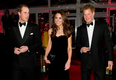 Prince William, Kate, and Prince Harry in formal attire at an event walking on a red carpet.