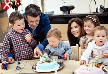 A family with young children gathered around a table with cakes, celebrating a birthday.