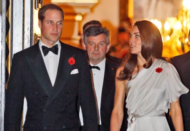 A man and a woman in formal attire, each wearing a red poppy, walk together at a gala event.