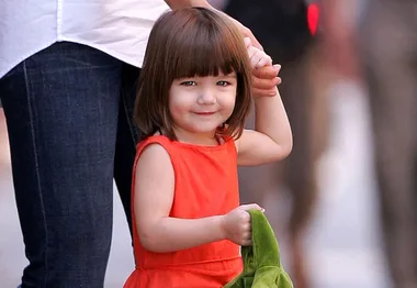 Child in an orange dress smiling and holding an adult's hand, with a green cloth in the other hand.