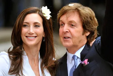 A couple smiling at their wedding, the bride with a flower in her hair, both dressed in formal attire.