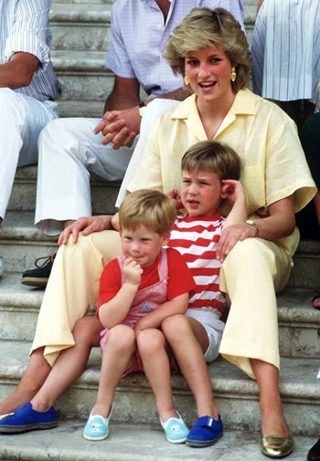 A woman in a yellow outfit sits on steps with two young boys in red and white outfits, smiling and relaxed.