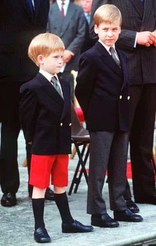 Two young boys in formal attire, one with red shorts, the other with gray pants, standing outside during an event.