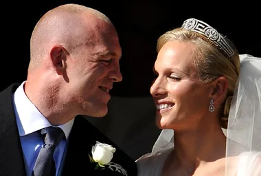 Zara Phillips and Mike Tindall smiling at their wedding, Zara wearing a tiara and veil, Mike in a suit with white rose boutonniere.
