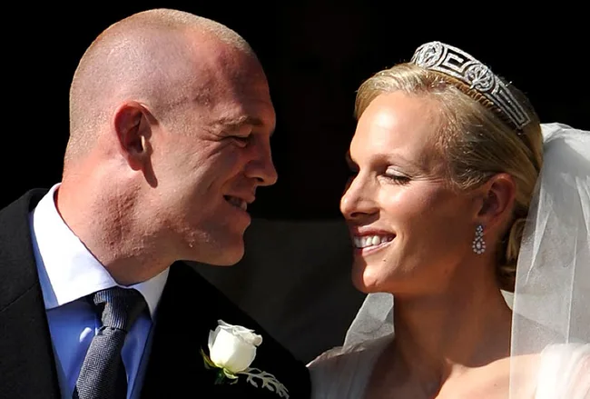 Zara Phillips and Mike Tindall smiling at their wedding, Zara wearing a tiara and veil, Mike in a suit with white rose boutonniere.