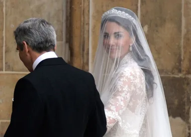 Bride in lace gown and veil with an escort at a wedding ceremony.