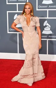 A person in an elegant beige gown poses on the red carpet at the Grammy Awards.