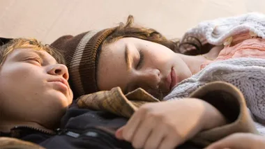 Two children peacefully sleeping, wearing warm clothing in soft light.